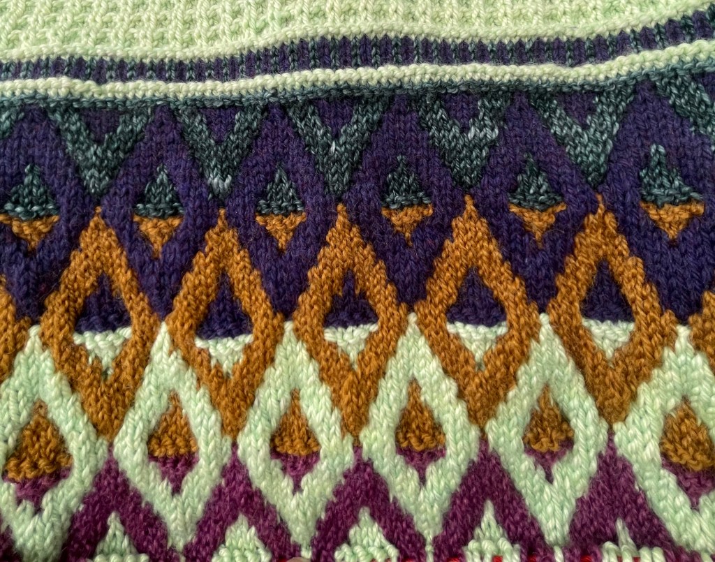 A close up of the striping diamond motif in dark green, dark purple, gold, the light green, and a light purple.