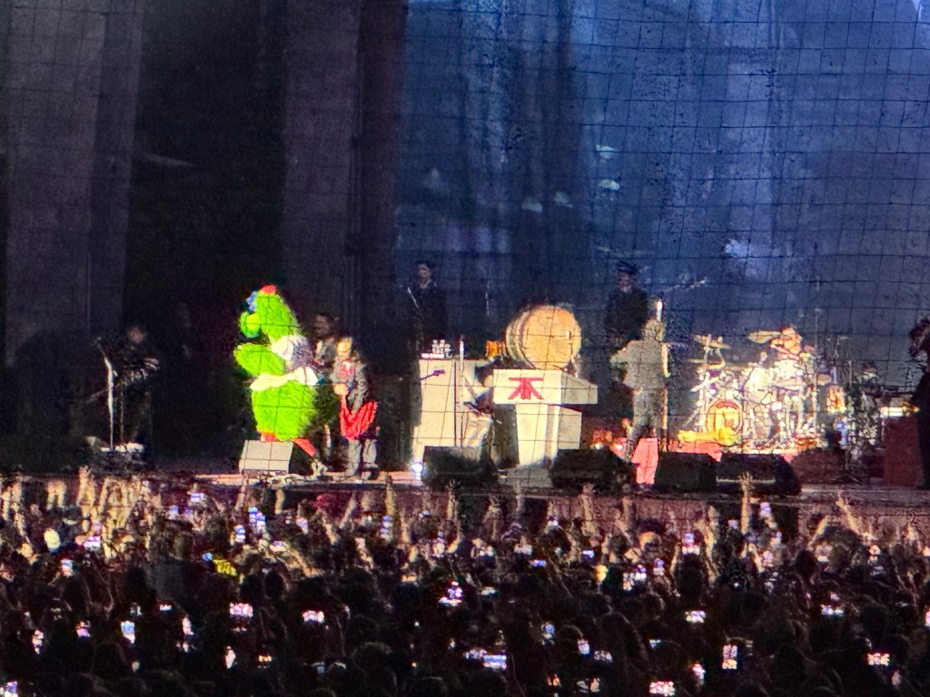 a closeup of the stage with all the band members, an actor, and the Philly Phanatic (a mascot who is tall, green, and fuzzy)