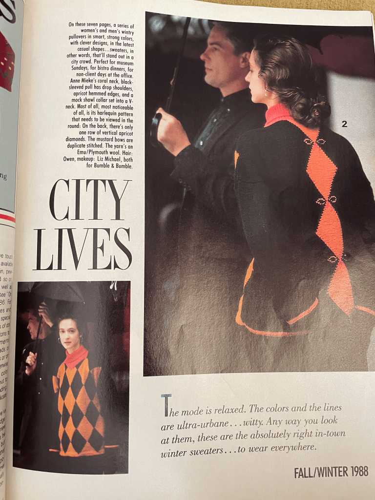 A page from the issue of Vogue Knitting where the Harlequin sweater is modeled. Int he main photo, the model is acing away from the camera and a single line of orange diamonds on a black background is shown on the back. There are duplicate stitch bows adorning the tops of the diamonds. In the inset image on the bottom left, the models faces the front, showing the grid of orange and black diamonds and a coral cowl neck. In both photos, the model is standing next to a man in a suit, holding an umbrella. The model is a white woman with brown hair, wearing gold hoop earrings.
